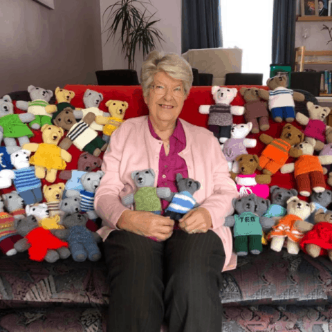 lady sitting on settee surrounded by knitted bears