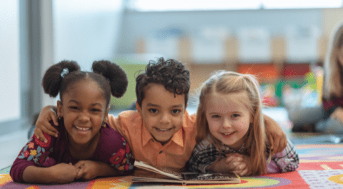 three children lying down in a line reading a book