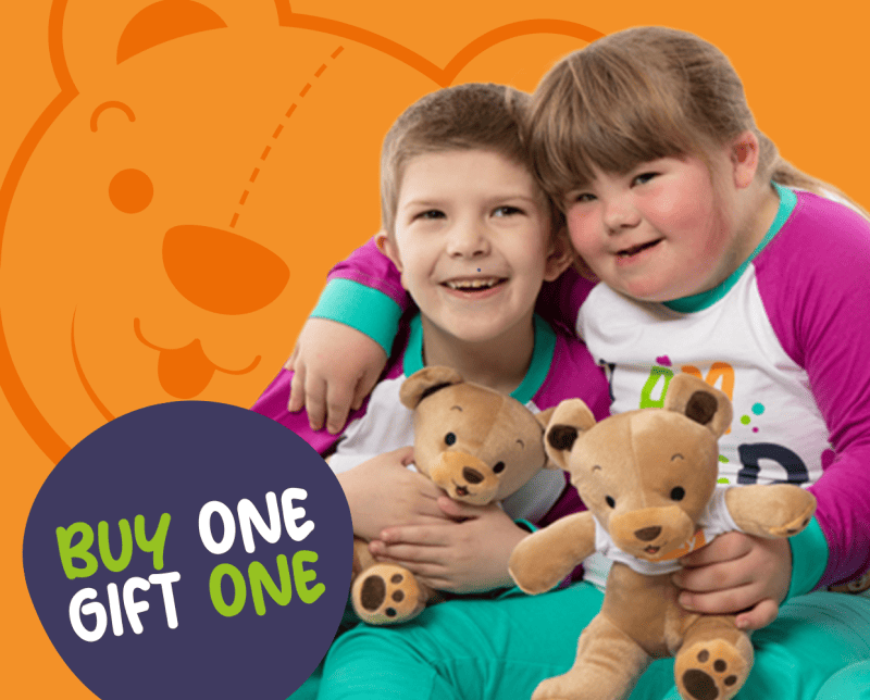 Young boy and girl wearing buddy bag pyjamas both hugging a teddy bear each, and hugging each other
